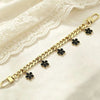 A delicate gold chain bracelet featuring black flower charms laid on a white lace fabric.