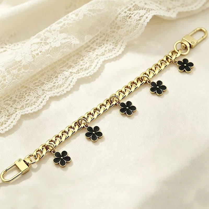 A delicate gold chain bracelet featuring black flower charms laid on a white lace fabric.