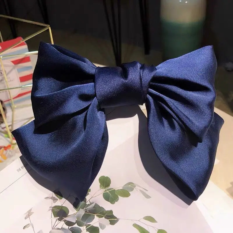 A dark blue silk bow hair clip used as a ponytail holder, displayed on a white surface.