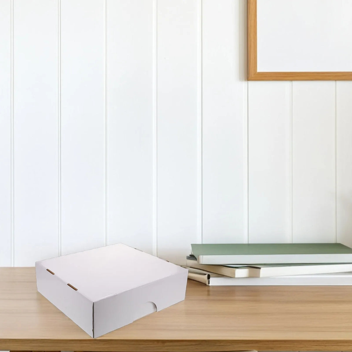 A white foldable trading card storage box resting on a wooden table next to some stacked books.