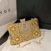 A gold rhinestone evening clutch with a crossbody strap resting on a white surface.