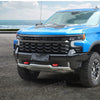 Blue Chevrolet Silverado front bumper with aftermarket tow hook cover installed.