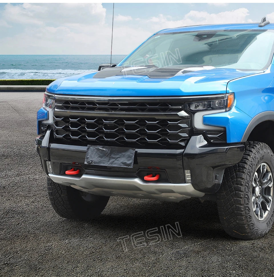 Blue Chevrolet Silverado front bumper with aftermarket tow hook cover installed.