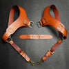 A pair of genuine brown leather double shoulder suspenders with brass buckles displayed against a dark background.