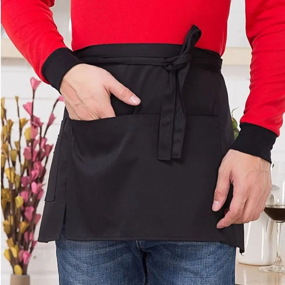 A black half apron with pockets is shown being worn by a person, featuring a red long-sleeved shirt.