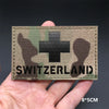 A rectangular tactical patch featuring a camouflage pattern with a black cross and the word SWITZERLAND on it.