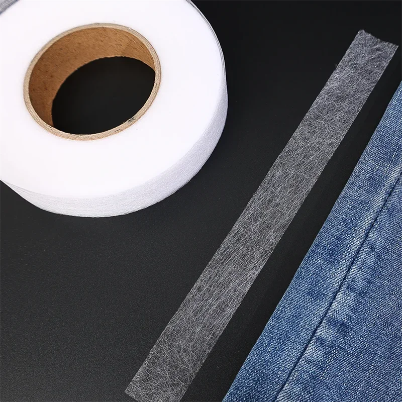 Roll of clear double-sided iron-on adhesive tape next to a piece of denim fabric