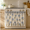 A white farmhouse oven skirt with a floral pattern and ruffle trim is installed on a stove.