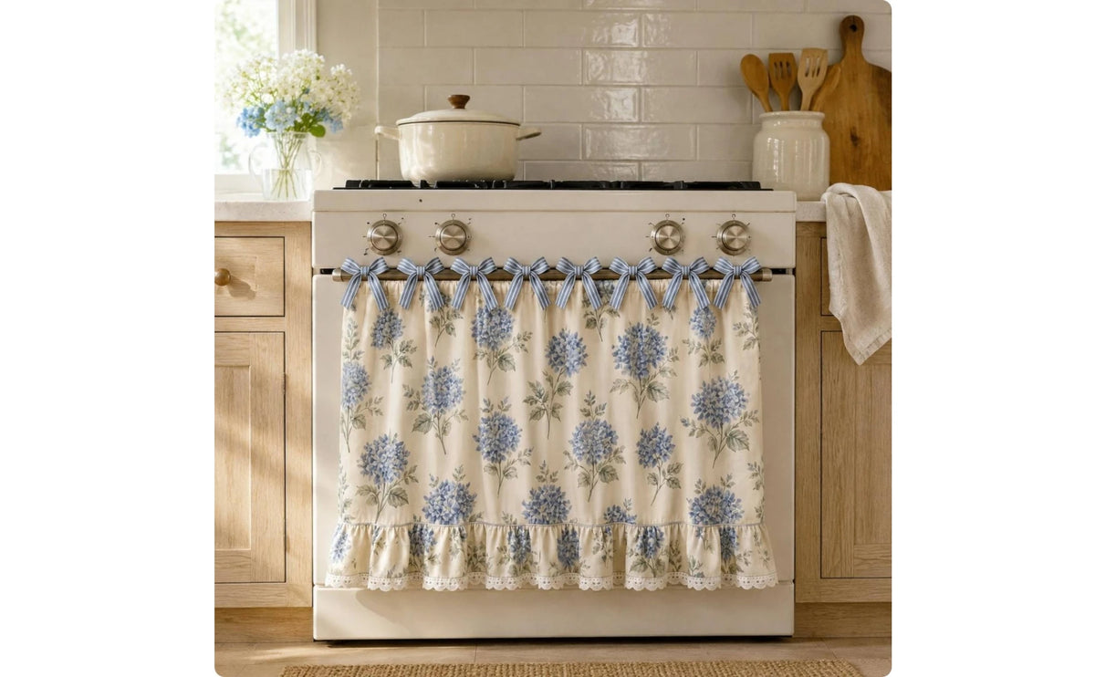 A white farmhouse oven skirt with a floral pattern and ruffle trim is installed on a stove.
