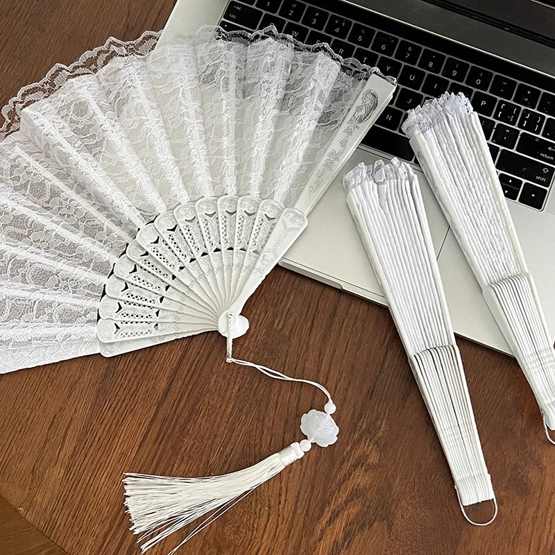 A white vintage lace folding hand fan with a delicate fan and a durable handle resting on a wooden surface.