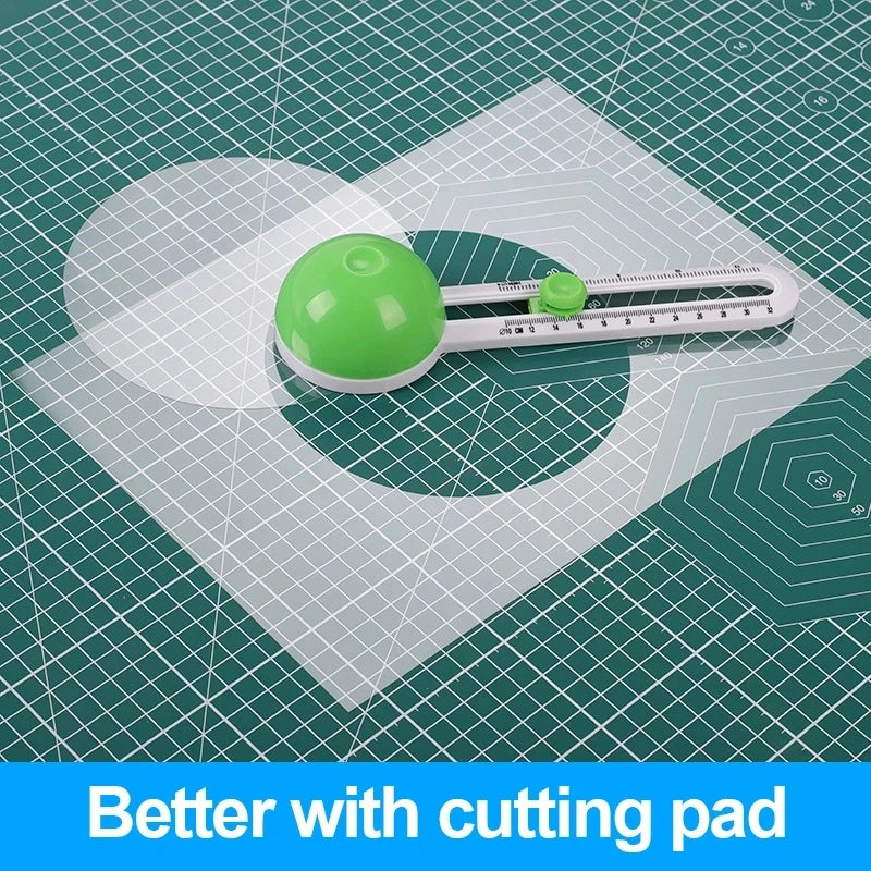 A green circular cutting pad and a white adjustable paper cutter are shown on a green grid surface.