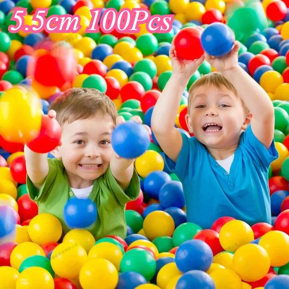 A child is holding red and blue soft play balls amidst a large pile of colorful balls.