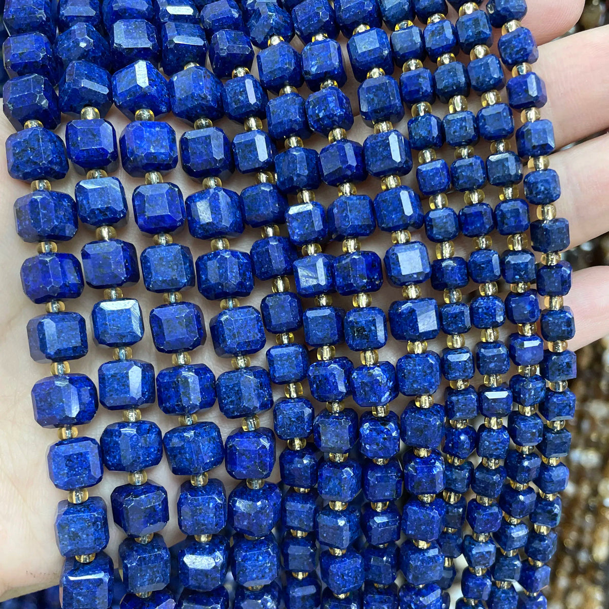A close-up of strands of deep blue natural stone square faceted beads for jewelry making
