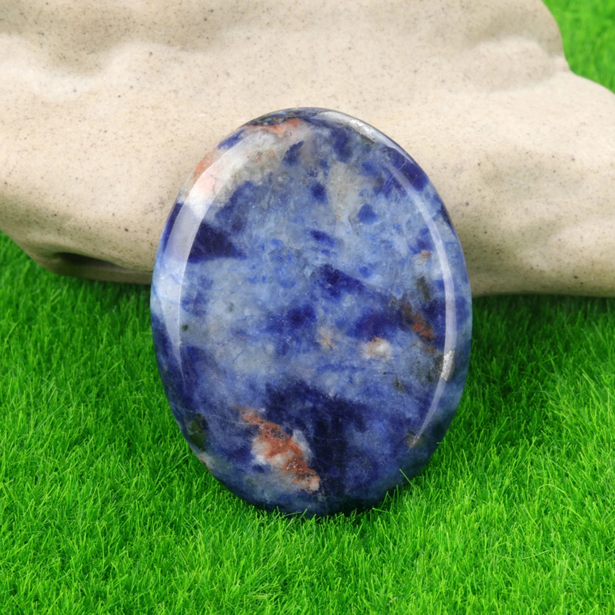 A smooth, oval blue and purple natural crystal stone resting on green grass.