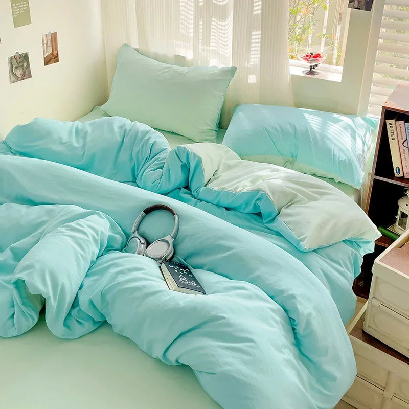 A light blue cotton bedding set featuring a flat sheet, duvet cover, and pillowcases displayed on a bed.