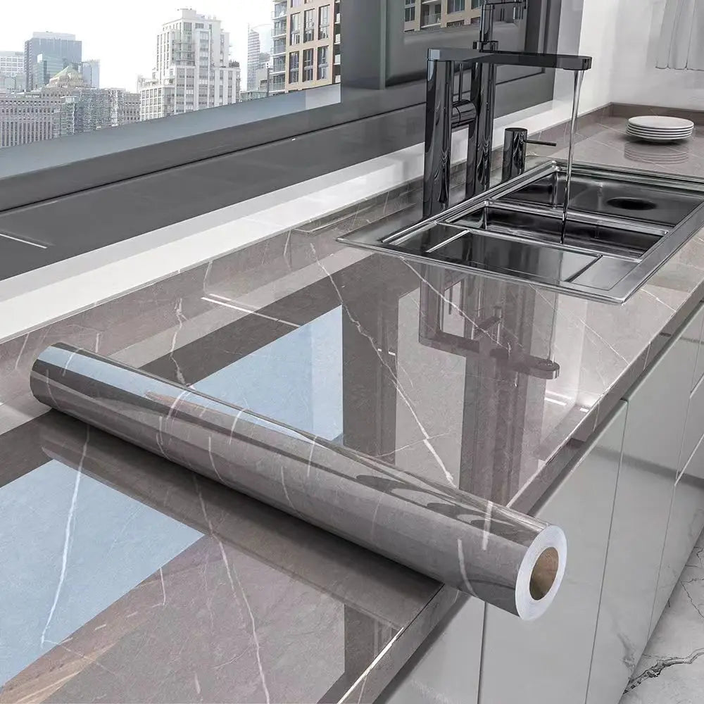A stainless steel kitchen sink and faucet installed in a marble-effect countertop, with a long roll of self-adhesive PVC film