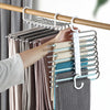 A hand is hanging a light gray knitted garment onto a multi-layered stainless steel pants hanger on a wooden rod.