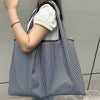 A woman holds a black and white striped foldable oxford cloth tote bag against a gray background.