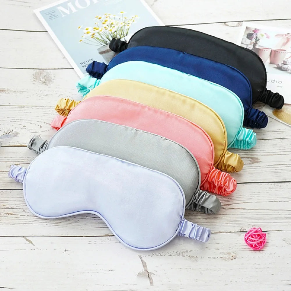 A stack of silk sleep masks in various pastel and dark colors laid on a white wooden surface.
