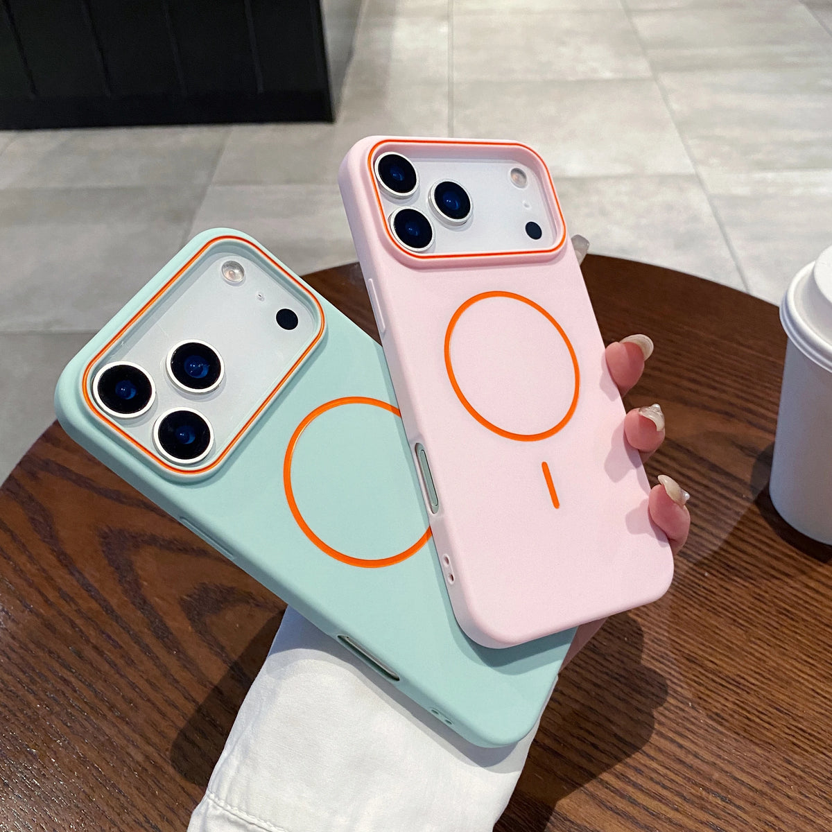A pink phone case with orange circular designs is displayed next to a light blue version on a wooden table.