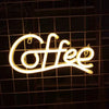 A glowing neon sign spelling out Coffee in cursive script mounted on a dark grid background.