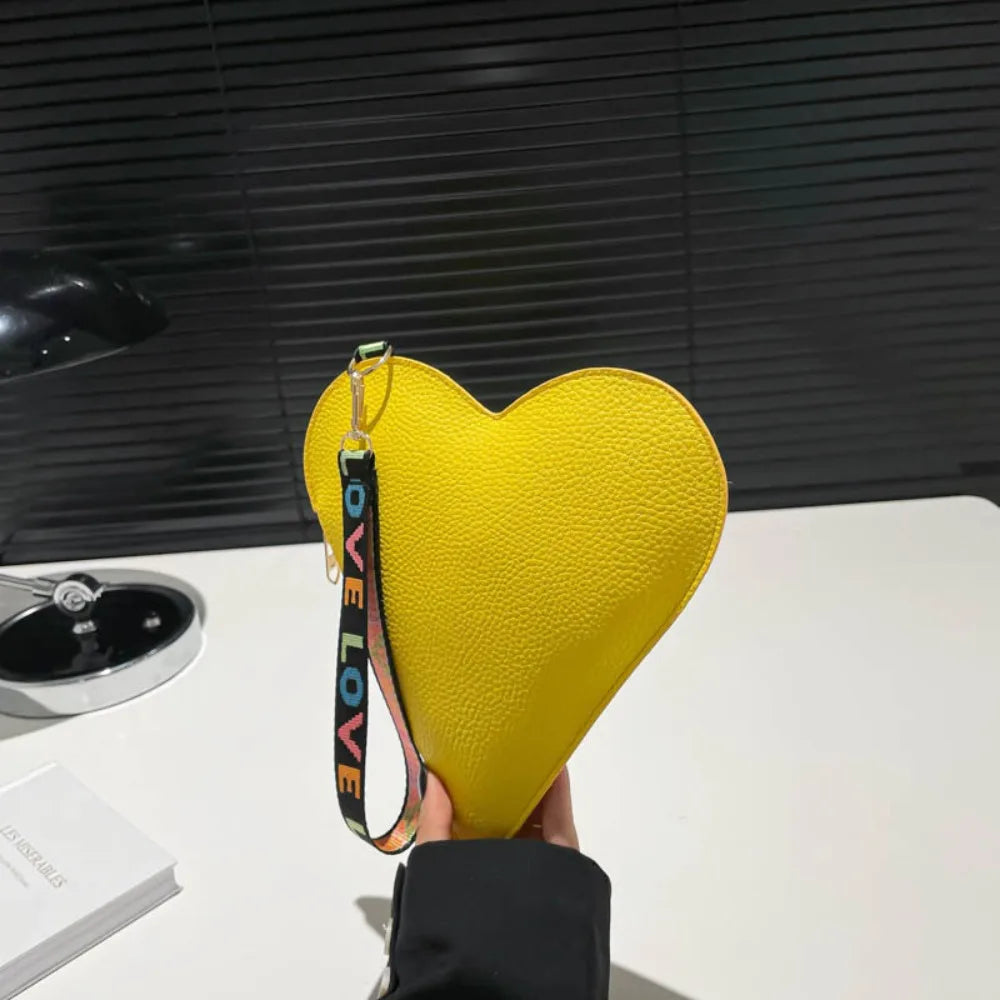 A bright yellow heart-shaped PU coin purse with a black wrist strap is displayed on a white surface.
