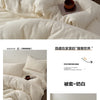 Ein Set faltiger weißer und lavendelfarbener Baumwoll-Duvetcover auf einem Bett.