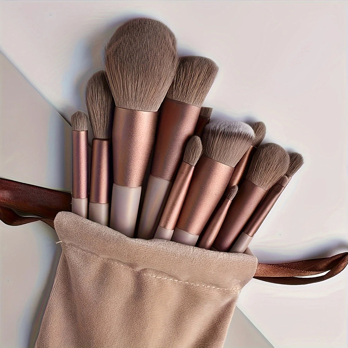 Set luxuriöser veganer Make-up-Pinsel in Roségold- und Nude-Tönen in einer beige Tasche.