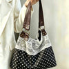 Sac à l'épaule noir et blanc à pois, avec un overlay en dentelle blanche et des sangles en cuir marron tenues par une personn