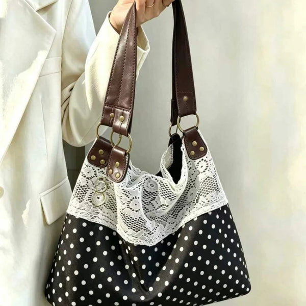 Sac à l'épaule noir et blanc à pois, avec un overlay en dentelle blanche et des sangles en cuir marron tenues par une personn