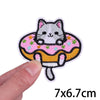 A white and black cartoon cat embroidery patch with pink and yellow floral accents being held by a hand.