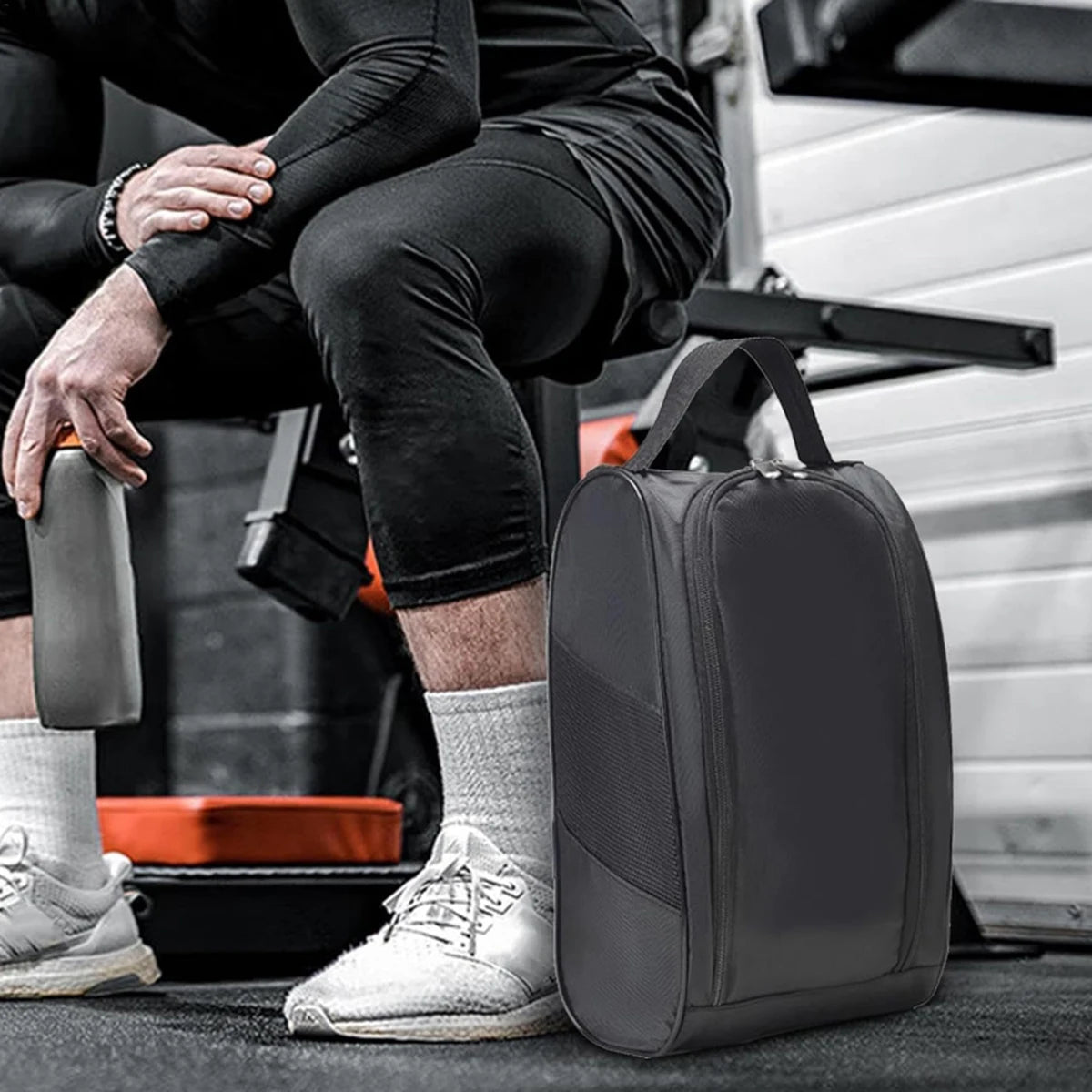 A dark gray breathable oxford cloth shoe storage bag resting on a black mat next to a person's legs.