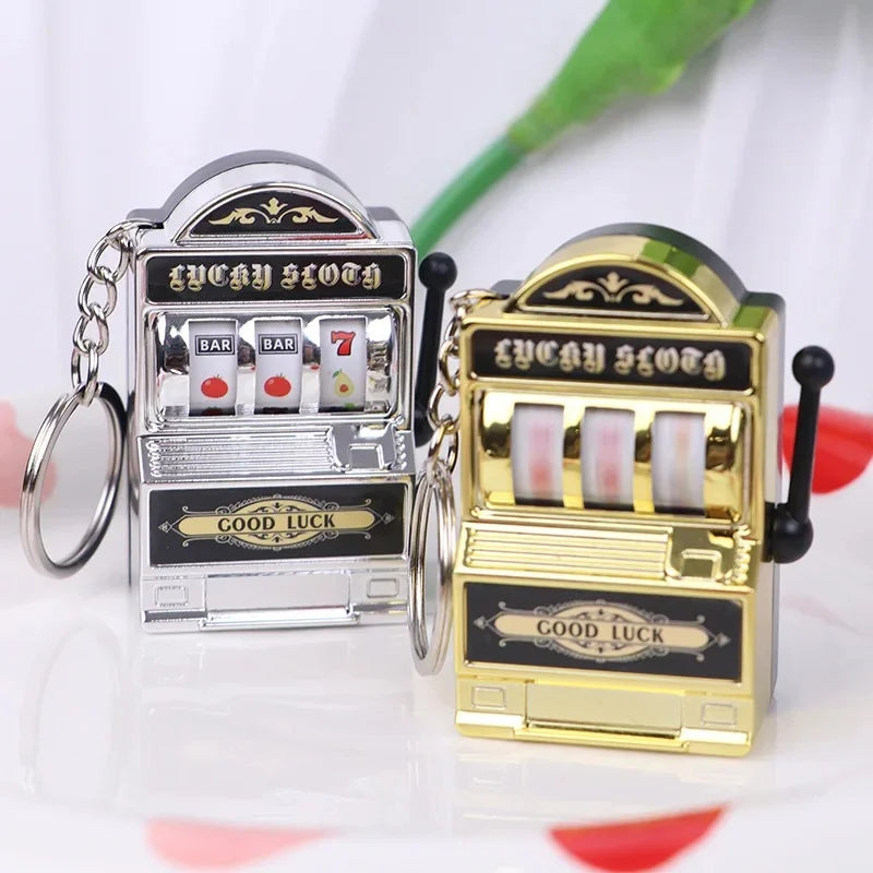 A silver and gold mini fruit slot machine keychain fidget toy with bars and a good luck sign.