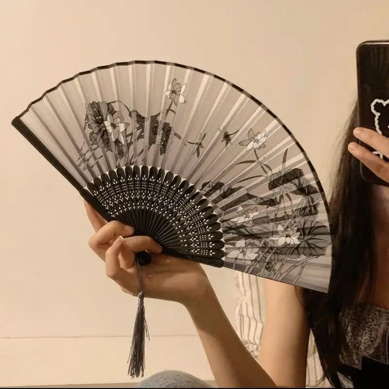A hand holds an open black and white bamboo and silk folding fan with a floral design.