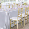 A long table set for a wedding or formal dining event with white satin tablecloths, gold chairs, and elegant place settings.