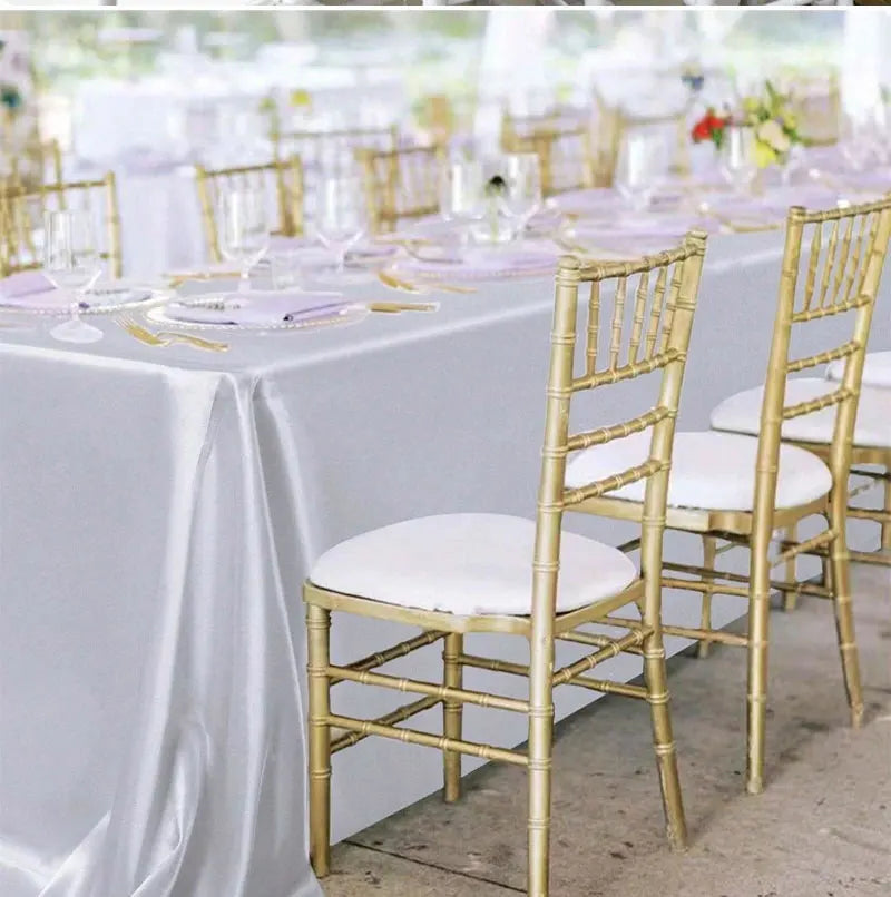 A long table set for a wedding or formal dining event with white satin tablecloths, gold chairs, and elegant place settings.