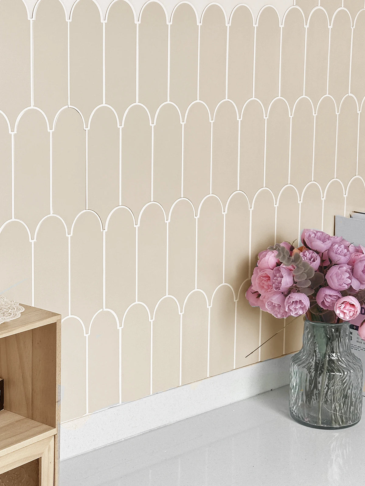 A beige wall with white arched tile molding and a vase of pink flowers.