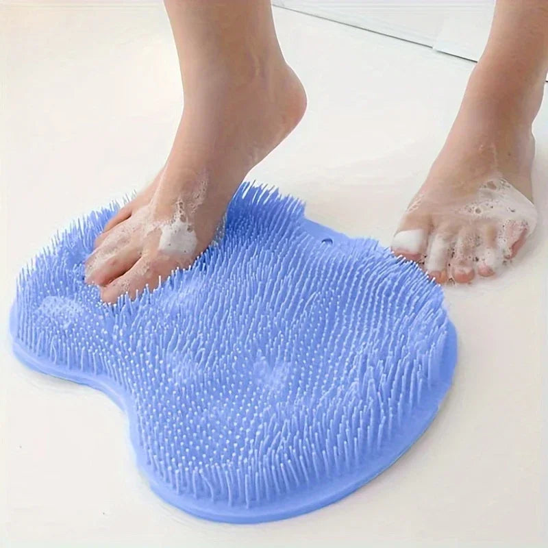 A hand is using a blue silicone shower mat with exfoliating bristles to wash feet.