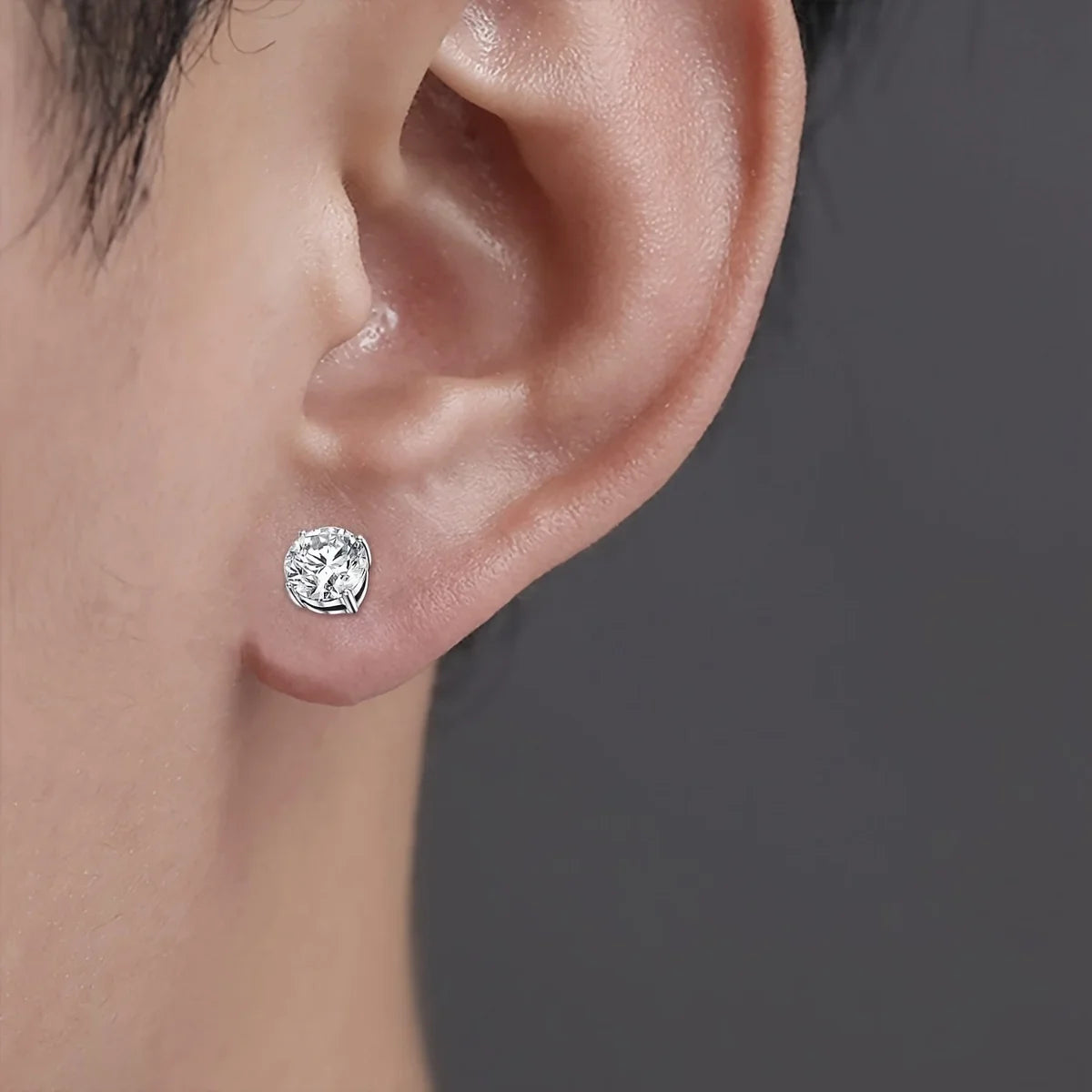 Gros plan d'un clou d'oreille magnétique rond en cristal argenté sur l'oreille d'une personne.