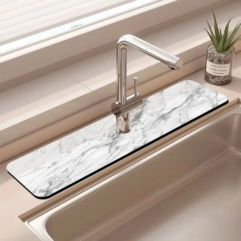 A modern kitchen sink features a marble drying mat and a chrome faucet with a plant in the background.