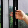 A hand is pulling open a black zippered self-adhesive mosquito net window screen.