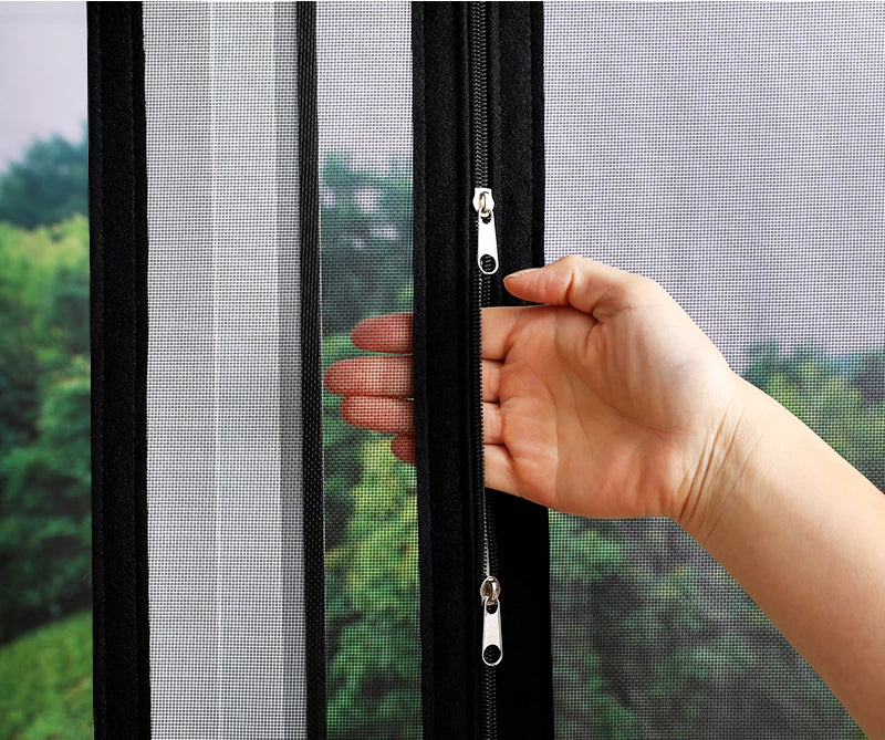 A hand is pulling open a black zippered self-adhesive mosquito net window screen.