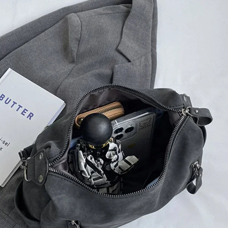 A gray vintage matte leather crossbody hobo bag with a zippered pocket revealing a black object.