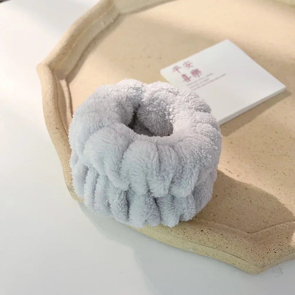 A light gray microfiber wrist sweatband and scrunchies are displayed on a beige tray next to a white card.
