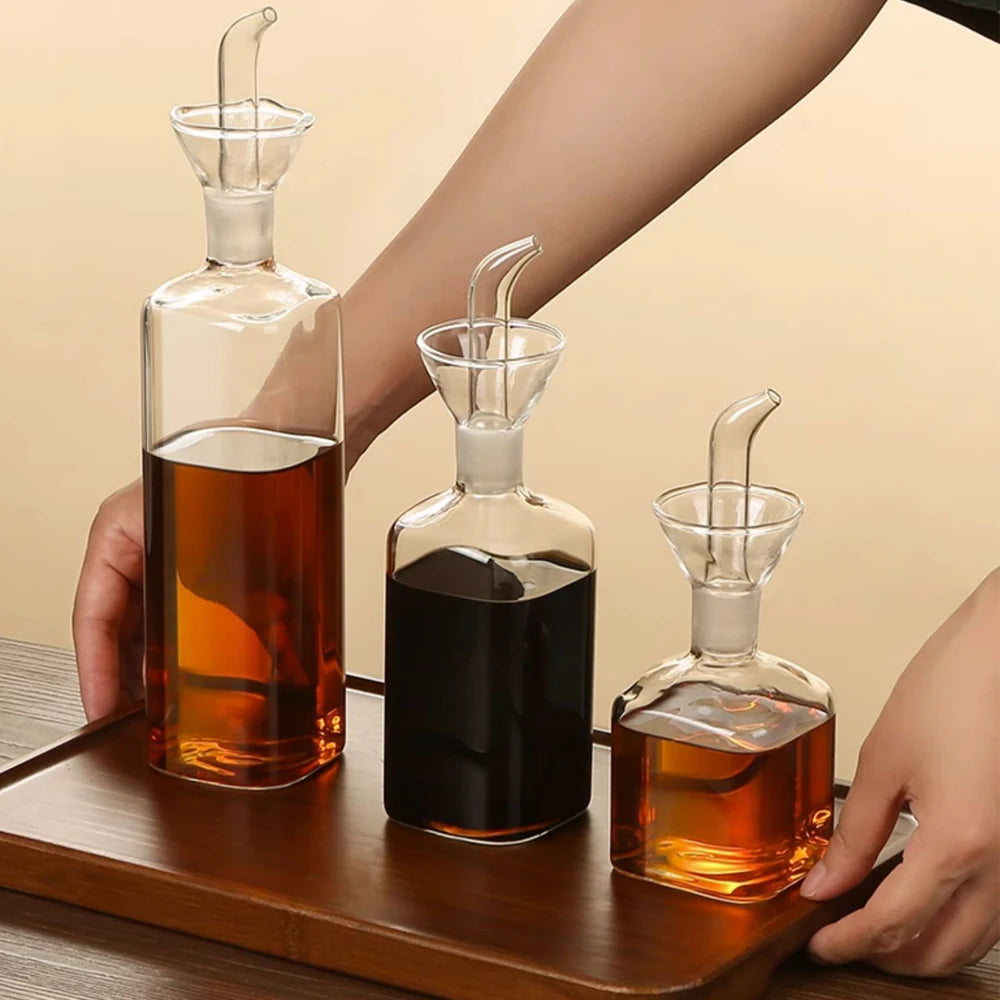 A hand holds a glass oil and vinegar dispenser with a dropper, showing various liquid levels.