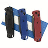 Three compact folding knives in black, blue, and red are displayed on a blue and white striped cloth.