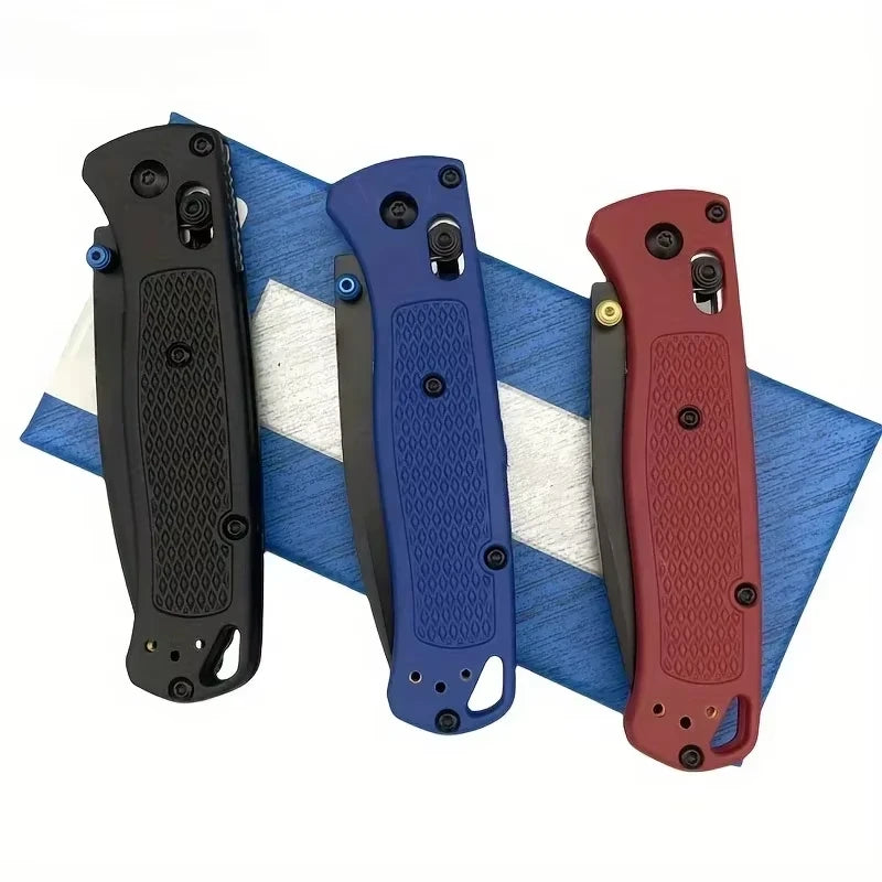 Three compact folding knives in black, blue, and red are displayed on a blue and white striped cloth.