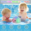 A baby is playing in the water with a light-up whale bath toy that sprays water.
