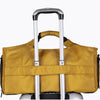 A tan duffel bag with a black trim and a shoe pocket is shown resting on a silver rolling suitcase.