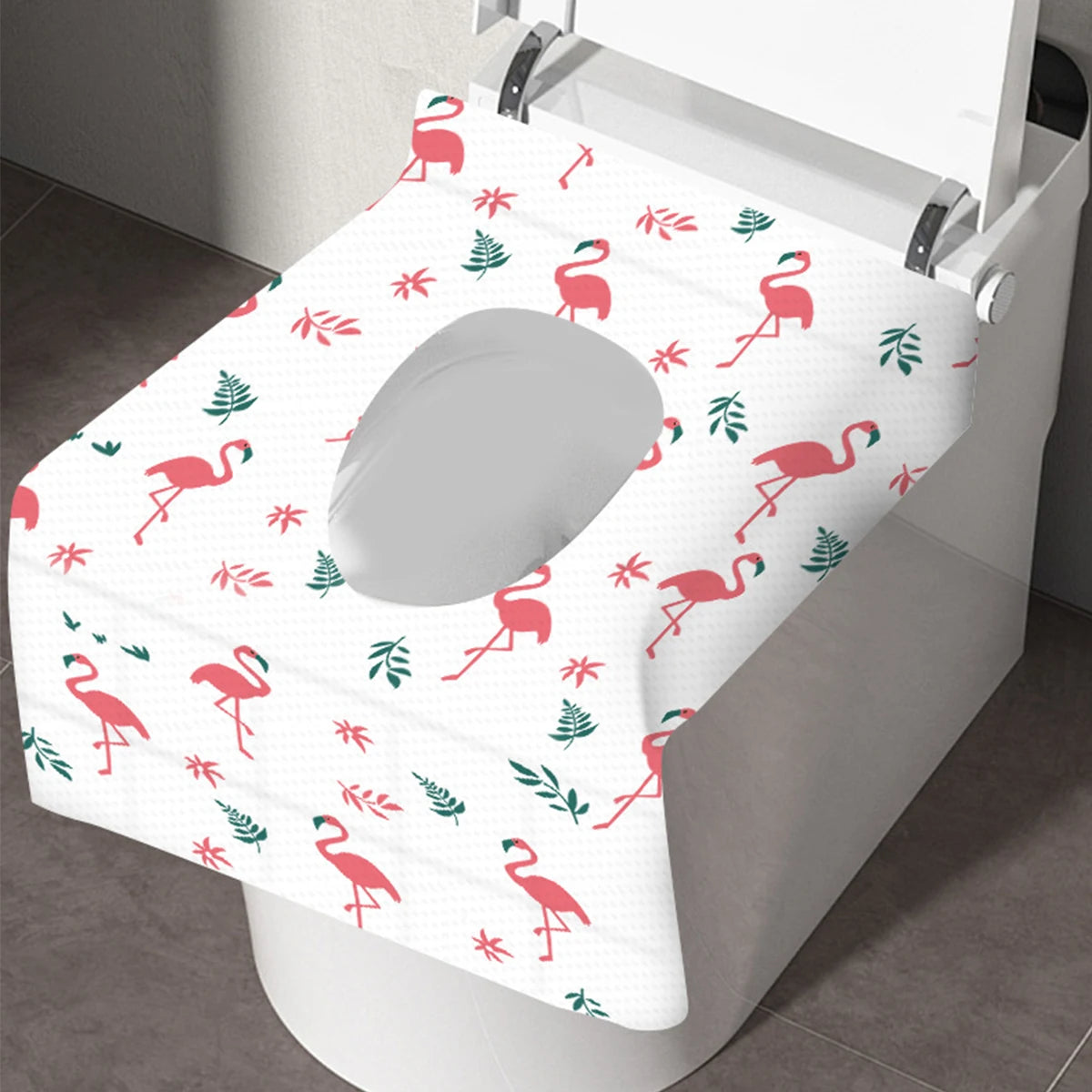 A white disposable toilet seat cover featuring a pattern of pink and green flamingos on a toilet seat.